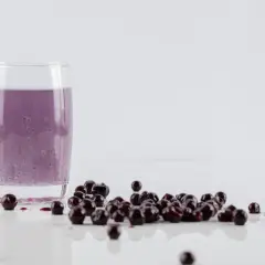 Szklanka orzeźwiającego soku z czarnej porzeczki z nasionami chia, obok świeżych owoców.
