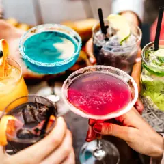Pięć kolorowych drinków z owocami i lodem, trzymanych przez ludzi.