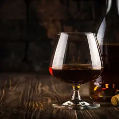Kieliszek brandy i butelka na drewnianym stole. Idealny moment, by zastanowić się, z czym pić brandy.