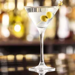 Kieliszek martini z dwiema oliwkami na wykałaczce na tle rozmytego baru.