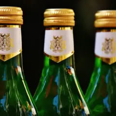 Trzy zielone butelki z złotymi nakrętkami i białymi etykietami z herbem.