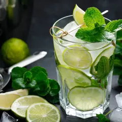 Szklanka orzeźwiającego mojito z limonką i miętą, otoczona lodem i składnikami.