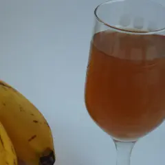 Dwa banany obok kieliszka z bursztynowym płynem.