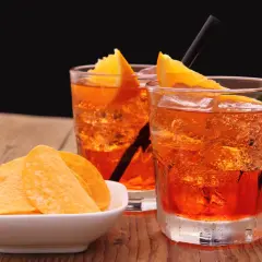 Dwa orzeźwiające drinki z pomarańczą i słomkami, obok miseczka chipsów. Idealny aperitif na letnie popołudnie.