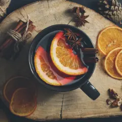 Kubek grzańca z pomarańczą, cynamonem i anyżem na drewnianej desce.