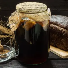 Słoik z ciemnym napojem, chleb żytni i kłosy zboża. Idealne składniki do domowego kwas chlebowy przepis.