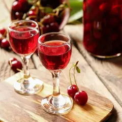 Dwa kieliszki z rubinowym winem z czereśni, obok świeże owoce i słoik pełen wiśni.