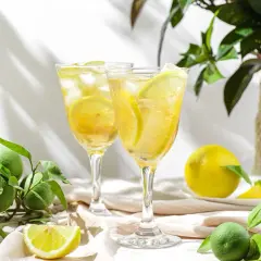 Orzeźwiający drink z limoncello, lodem i plasterkami cytryny, otoczony świeżymi owocami i zielonymi liśćmi.