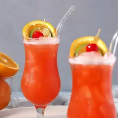 Dwa drinki z rumem, ozdobione plasterkami pomarańczy, limonki i wiśnią, z owocami w tle.