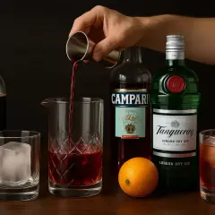 Składniki do koktajlu: gin, Campari, wermut, pomarańcza, lód i ciemny płyn.