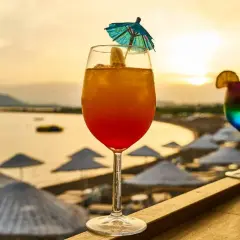Dwa kolorowe drinki na tle plaży i zachodzącego słońca.