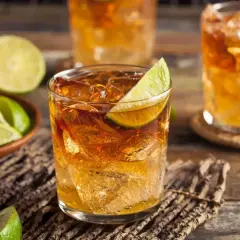 Szklanki z drinkami rumowymi z lodem i limonką, obok miseczka z ćwiartkami limonki.