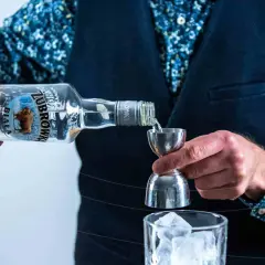 Barman nalewa wódkę Żubrówka Biała z butelki do jiggera nad szklankę z lodem.