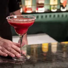 Mrożona czerwona margarita w kieliszku z solą na brzegu, podawana przez barmana.