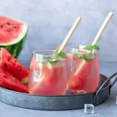 Dwa orzeźwiające koktajle z arbuzem i miętą na tacy, obok kawałków arbuza i kostek lodu.