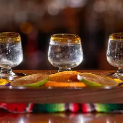 Trzy kieliszki z mezcalem, plasterki limonki i pomarańczy na drewnianej desce.