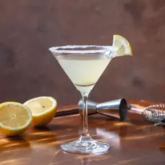 Koktajl Martini Bianco w kieliszku z solą na brzegu, udekorowany plasterkiem cytryny, obok cytryny i oliwki.