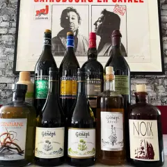 Butelki z zielonymi likierami Chartreuse i innymi francuskimi alkoholami na tle plakatu.