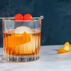 Klasyczny koktajl Old Fashioned z pomarańczą i wisienkami na patyczku.