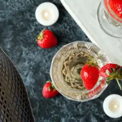Butelka i kieliszki pełne musującego prosecco, ozdobione truskawkami i świecami. Idealne na romantyczny wieczór.