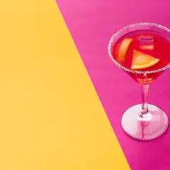 Elegancki kieliszek z czerwonym drinkiem, ozdobiony plasterkami pomarańczy i cukrowym rantem, idealny na wieczór w stylu cosmopolitan.