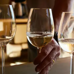 Trzy kieliszki z białym winem, jedno trzymane przez dłoń z obrączką.
