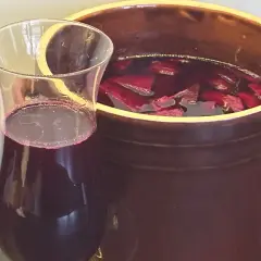 Szklanka z ciemnoczerwonym płynem obok glinianego naczynia z kawałkami buraków. To domowy zakwas z buraków, gotowy do spożycia.