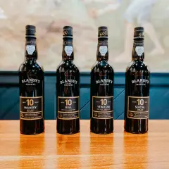 Cztery butelki wina madera, każda z 10-letnim oznaczeniem, stoją na drewnianym stole.