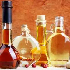 Cztery butelki z płynami: ciemny alkohol, jasny płyn z owocami, złoty olej i miodówka.