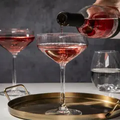 Różowe prosecco nalewane do kieliszka na tacy, obok inne kieliszki i szklanka z wodą.