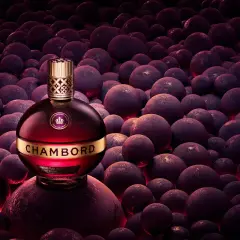 Elegancka butelka likieru Chambord wśród ciemnych, okrągłych owoców, emanująca luksusem i bogactwem smaku.