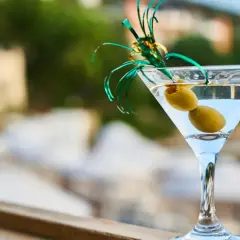 Orzeźwiający martini fiero z oliwkami, ozdobiony zieloną wstążką, na tle rozmytego, letniego krajobrazu.