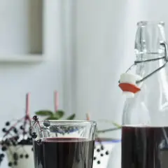 Szklanka i butelka z ciemnym sokiem z czarnego bzu, ozdobione gałązkami z owocami.