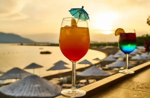 Dwa kolorowe drinki na tle plaży i zachodzącego słońca.