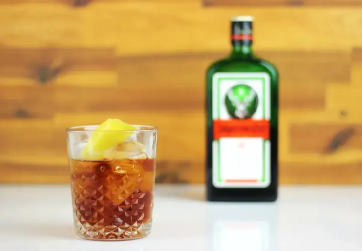 Szklanka z drinkiem i cytryną obok butelki Jägermeister. Ten jager alkohol to idealny dodatek do wieczoru.