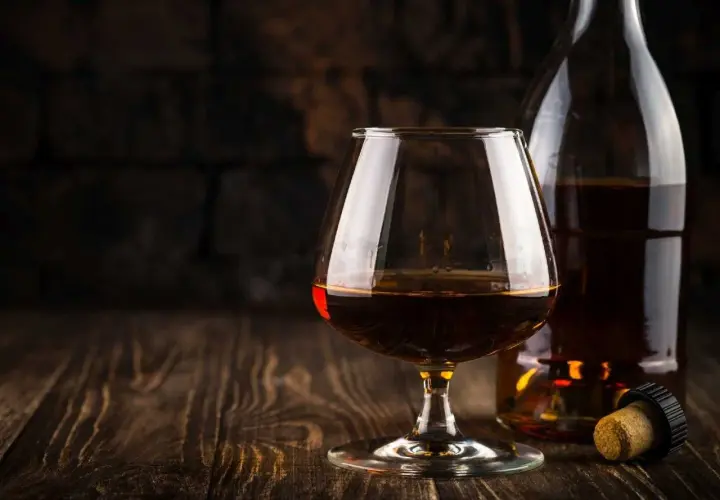Kieliszek brandy i butelka na drewnianym stole. Idealny moment, by zastanowić się, z czym pić brandy.