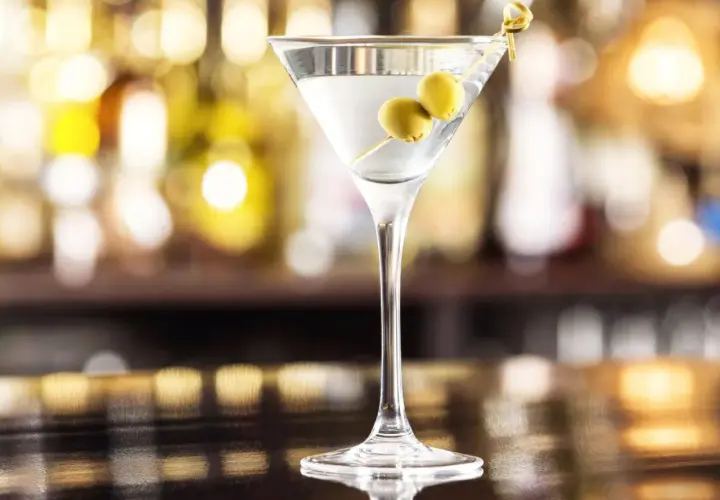 Kieliszek martini z dwiema oliwkami na wykałaczce na tle rozmytego baru.