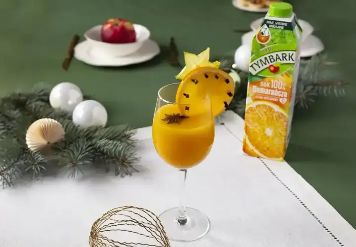 Pomarańczowy koktajl w kieliszku, ozdobiony plasterkiem pomarańczy z goździkami i gwiazdką anyżu.
