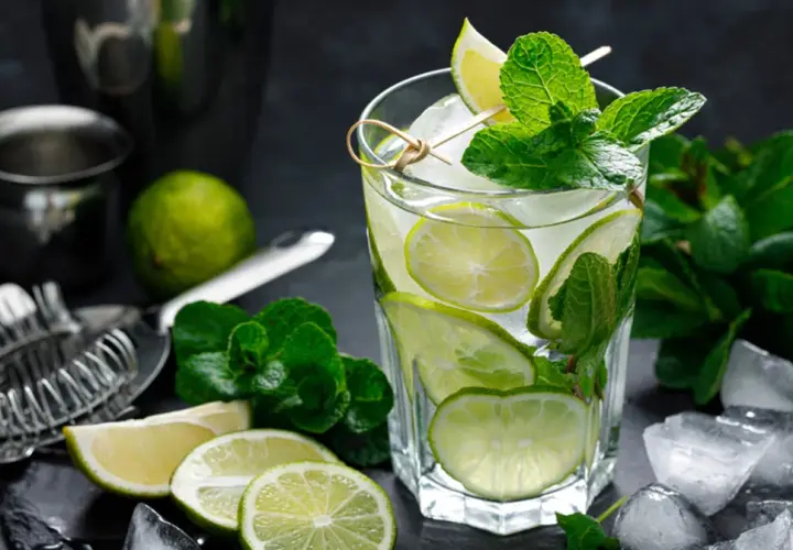 Szklanka orzeźwiającego mojito z limonką i miętą, otoczona lodem i składnikami.