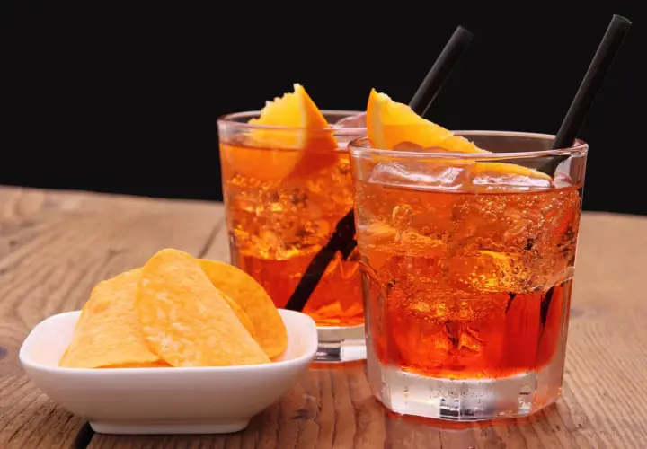 Dwa orzeźwiające drinki z pomarańczą i słomkami, obok miseczka chipsów. Idealny aperitif na letnie popołudnie.