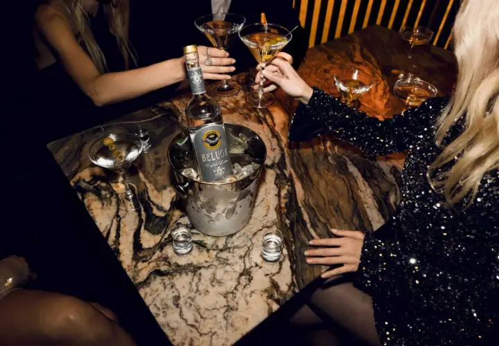 Butelka wódki Beluga w wiaderku z lodem, kieliszki z martini i shoty na marmurowym stole.