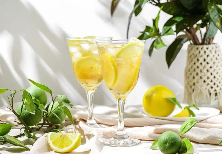 Orzeźwiający drink z limoncello, lodem i plasterkami cytryny, otoczony świeżymi owocami i zielonymi liśćmi.