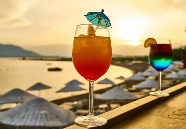 Dwa kolorowe drinki na tle plaży i zachodzącego słońca.