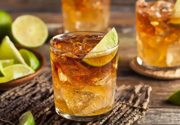 Szklanki z drinkami rumowymi z lodem i limonką, obok miseczka z ćwiartkami limonki.