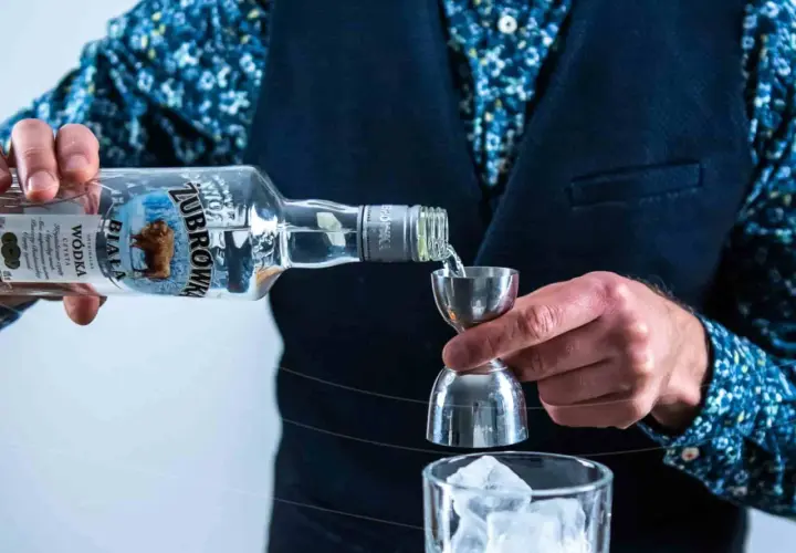 Barman nalewa wódkę Żubrówka Biała z butelki do jiggera nad szklankę z lodem.