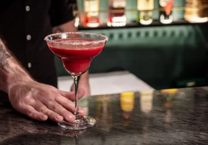 Mrożona czerwona margarita w kieliszku z solą na brzegu, podawana przez barmana.