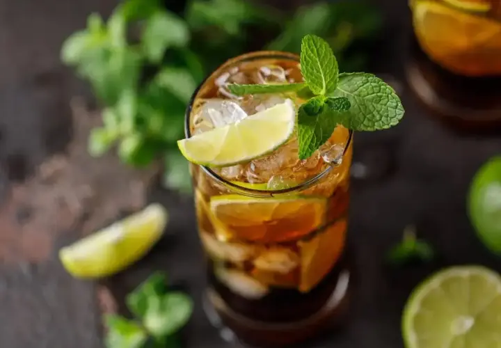 Szklanka z drinkiem z rumu Bacardi, lodem, plasterkami limonki i listkami mięty.