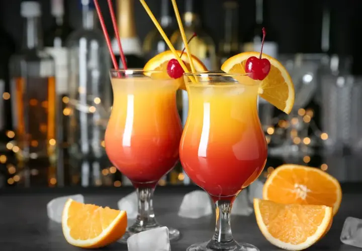 Dwa drinki z wódką w kieliszkach z pomarańczą i wiśnią, na tle baru.