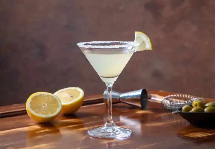Koktajl Martini Bianco w kieliszku z solą na brzegu, udekorowany plasterkiem cytryny, obok cytryny i oliwki.
