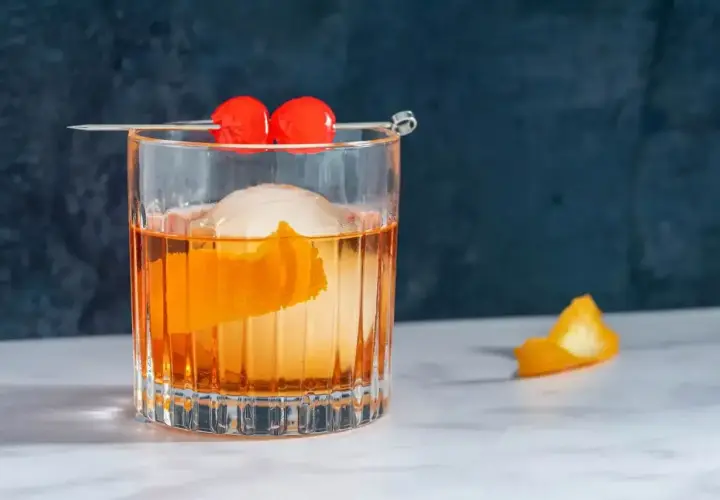 Klasyczny koktajl Old Fashioned z pomarańczą i wisienkami na patyczku.